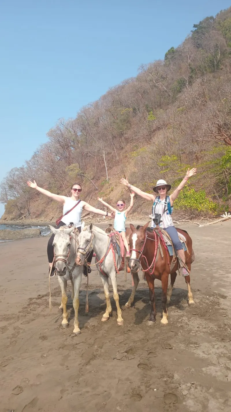 Three riders on a sunny Jacó beach horseback ride with jungle hills behind